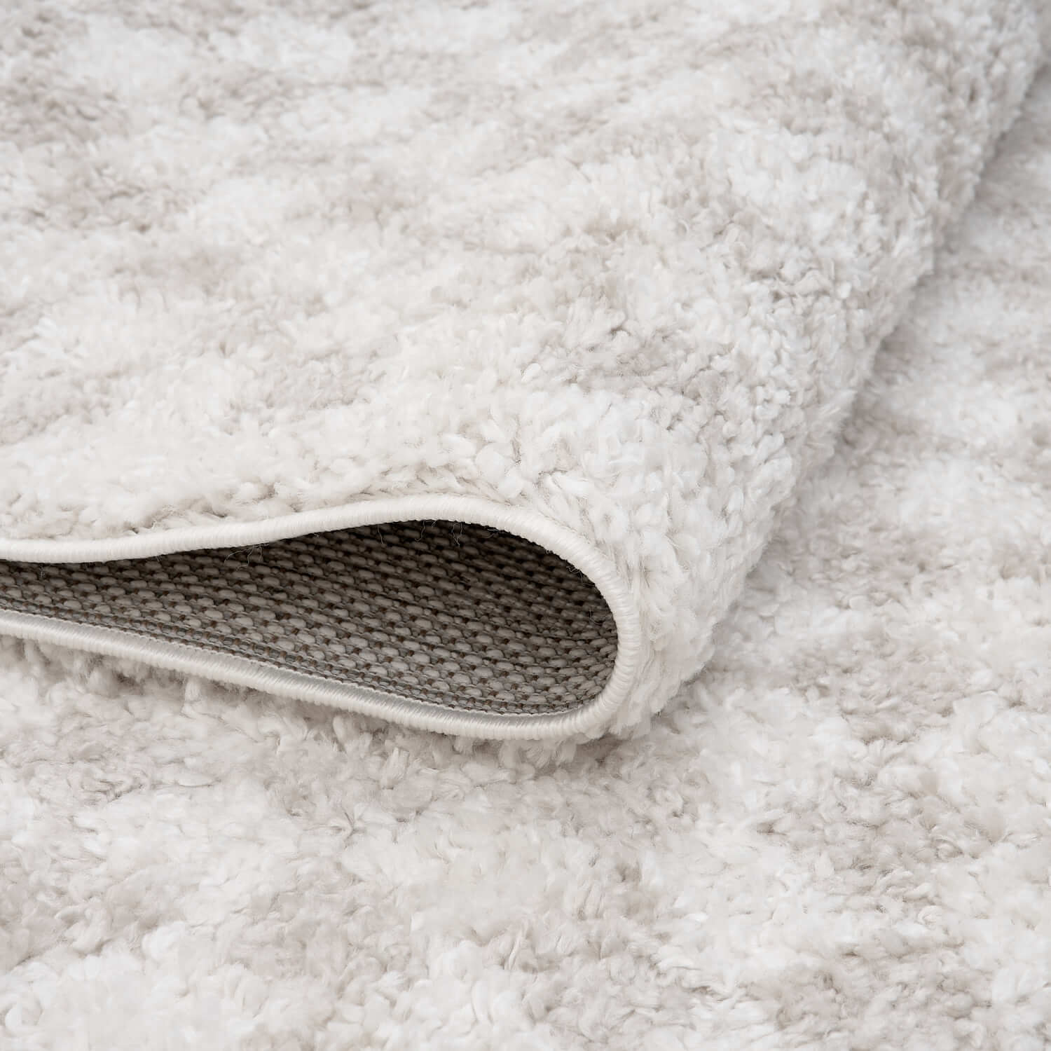 Light beige Moodi Nomari shaggy runner rug by The Rugs, folded to show its soft, textured shaggy surface and durable design.