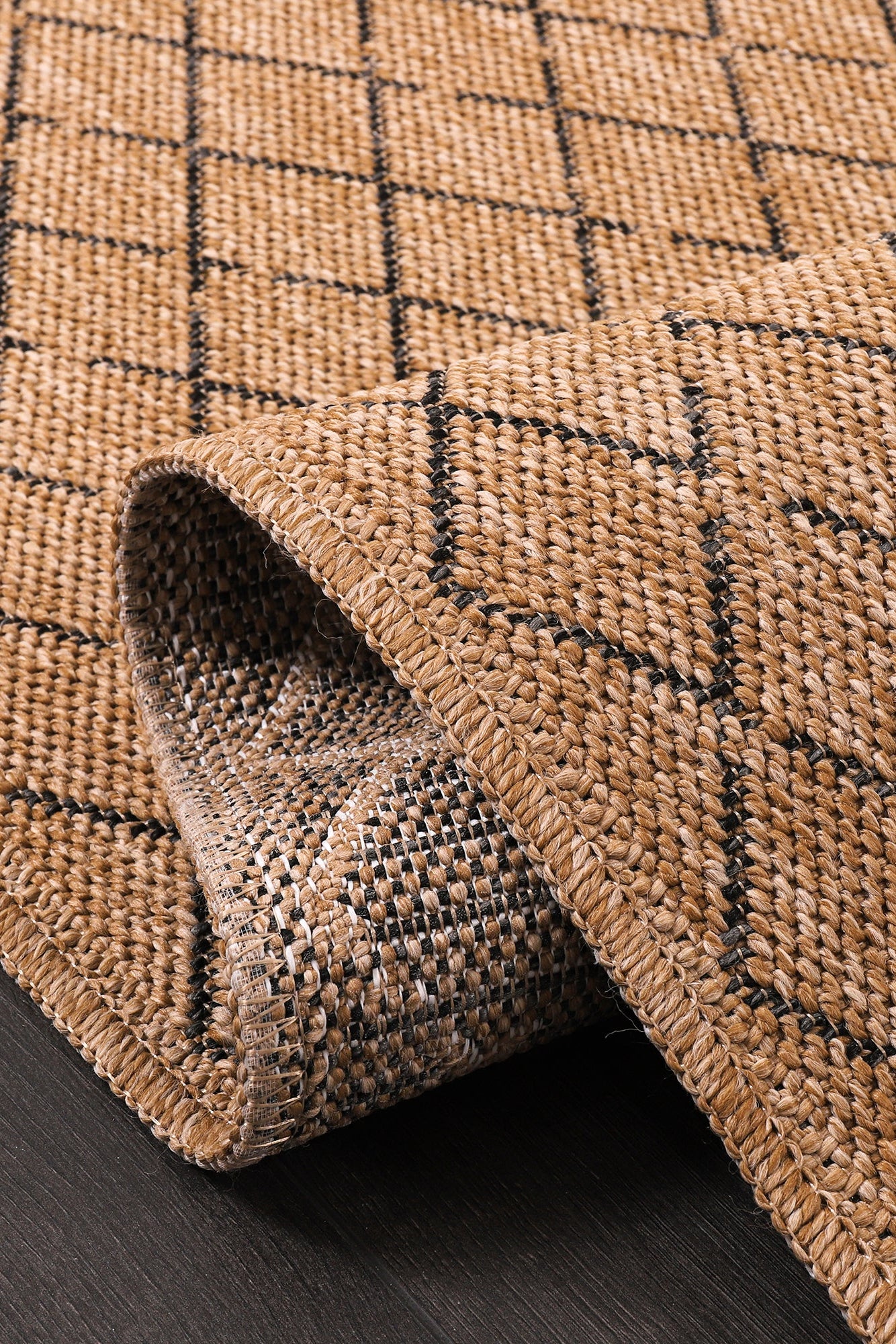 Brown woven rug with black geometric pattern on a dark wooden floor